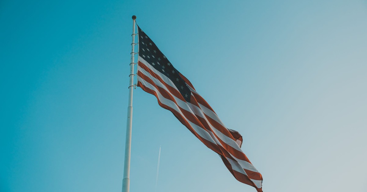 Low angle view of American flag waving on a flagpole against a bright clear sky.