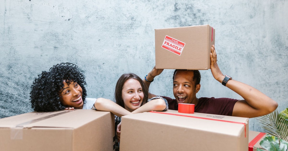 Diverse group of friends smiling while packing moving boxes. Relocation and new beginnings.