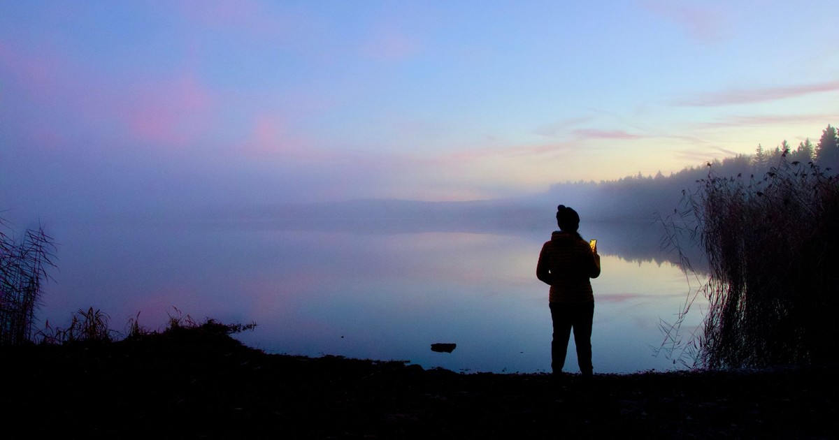 Silhouette of a person by a misty lake at twilight with a serene and tranquil atmosphere.