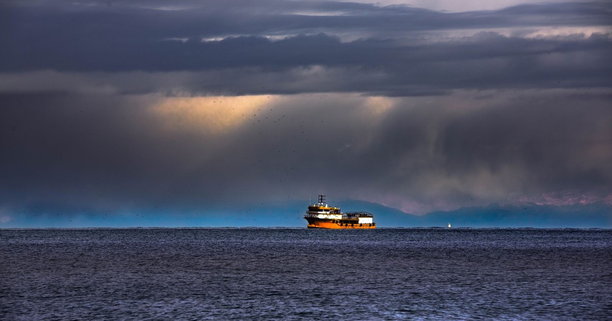A solitary ship navigates the vast ocean under dramatic, stormy clouds at sea.