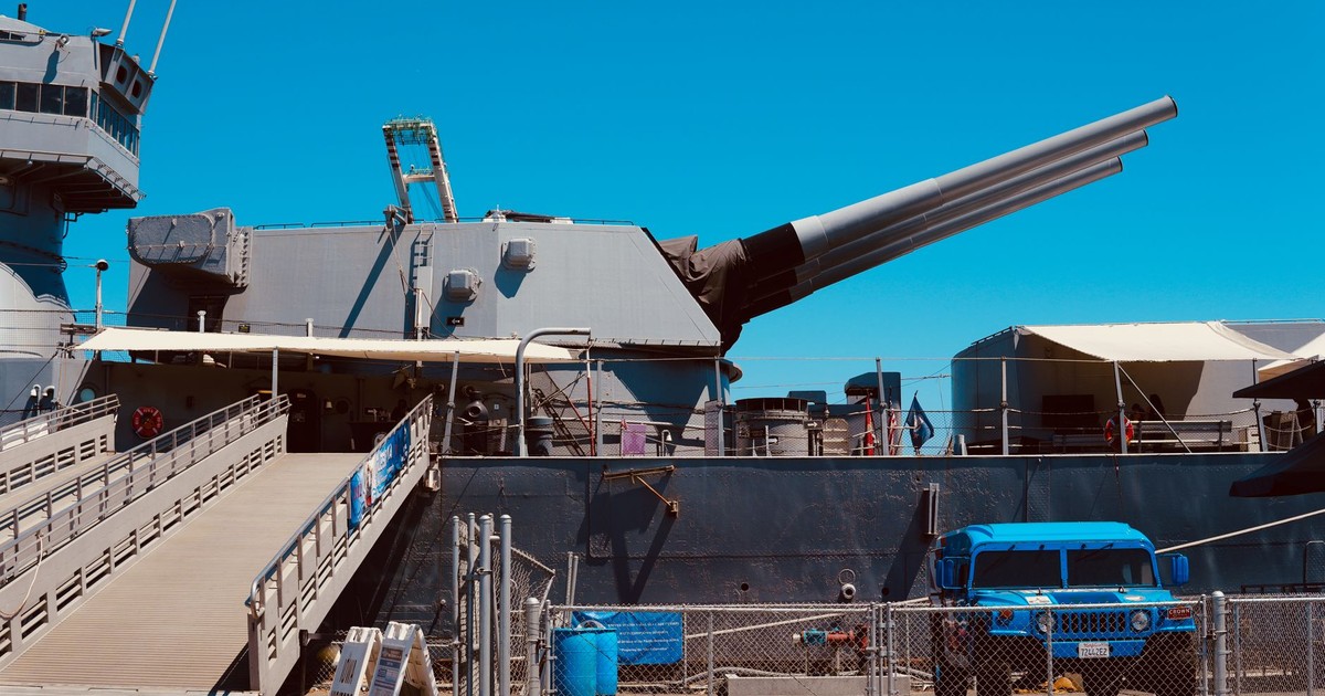 A towering battleship with cannons docked at Los Angeles harbor on a clear day.