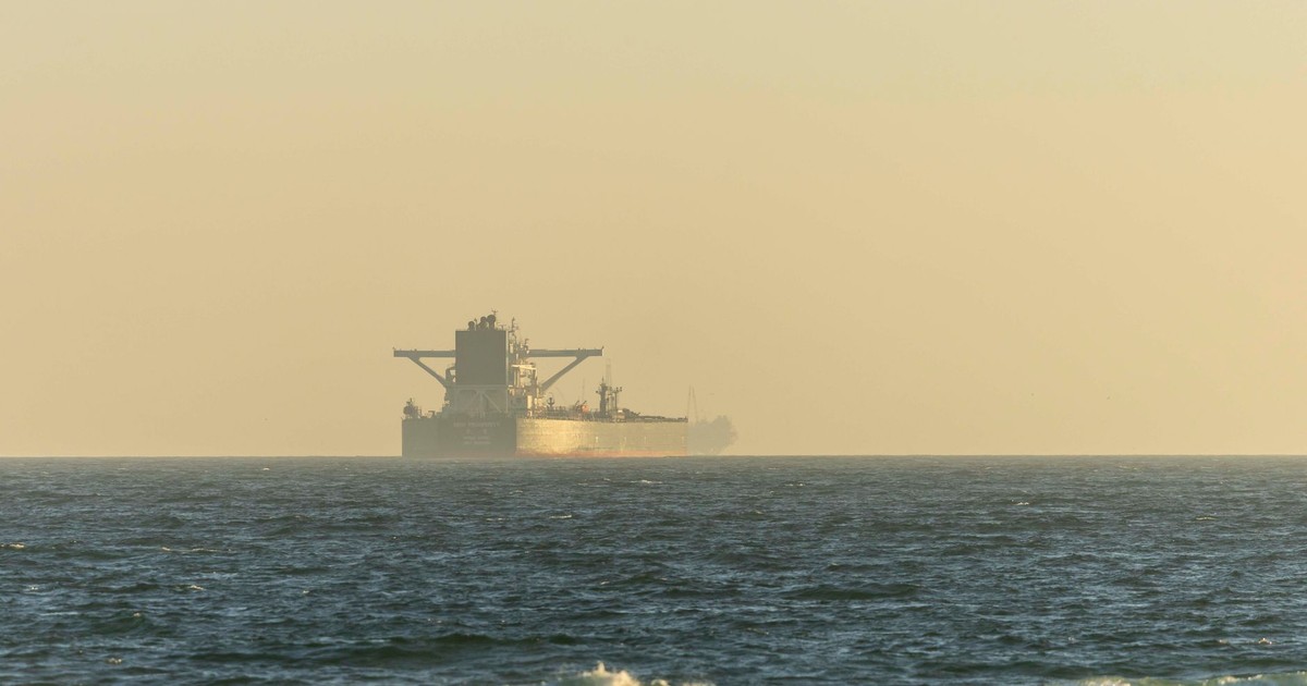 A cargo ship silhouetted against the horizon on a calm ocean during twilight.
