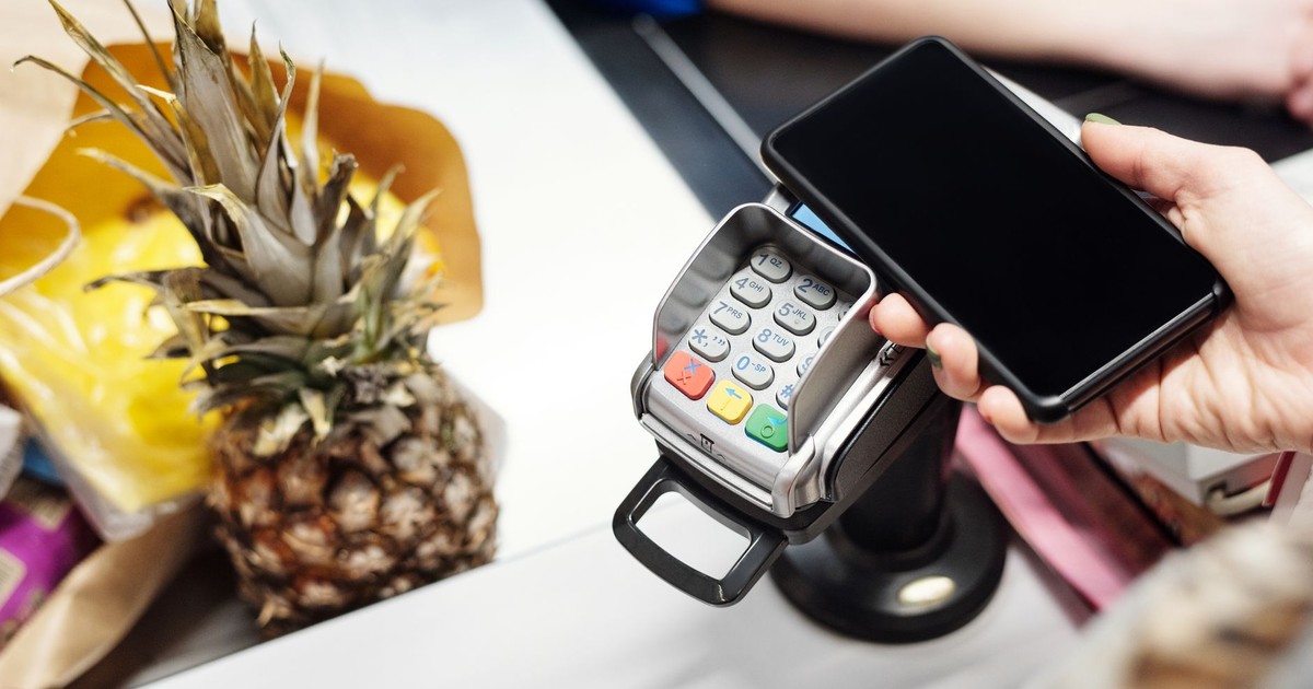 Close-up of a customer using a smartphone for contactless payment at a retail checkout with a pineapple on the counter.