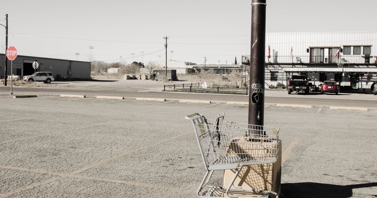 A lone shopping cart in a deserted parking lot under a clear sky.