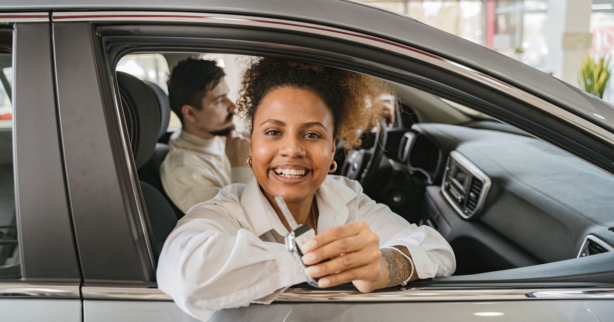 Joyful couple in their new car, holding keys in a dealership showroom, smiling warmly.