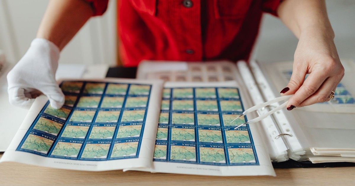 A person wearing gloves carefully handling a collection of vintage postage stamps using tweezers.