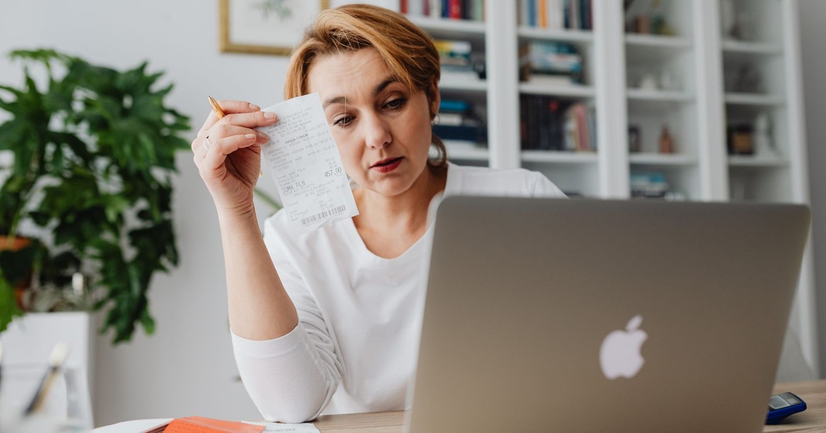Woman concentrating on receipts while using a laptop, reflecting financial stress.