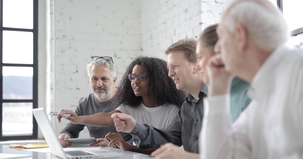 Content African American female worker pointing at netbook screen while speaking about project with diverse colleagues and sitting at white table in office in sunlight