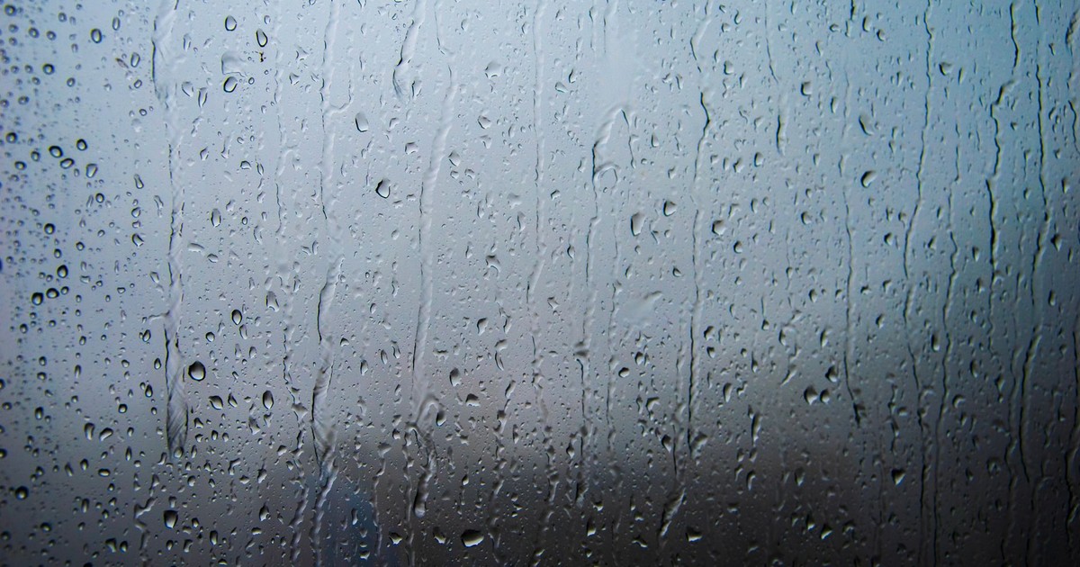 Rain-covered window with visible droplets and streaks creating a textured surface and moody ambiance.