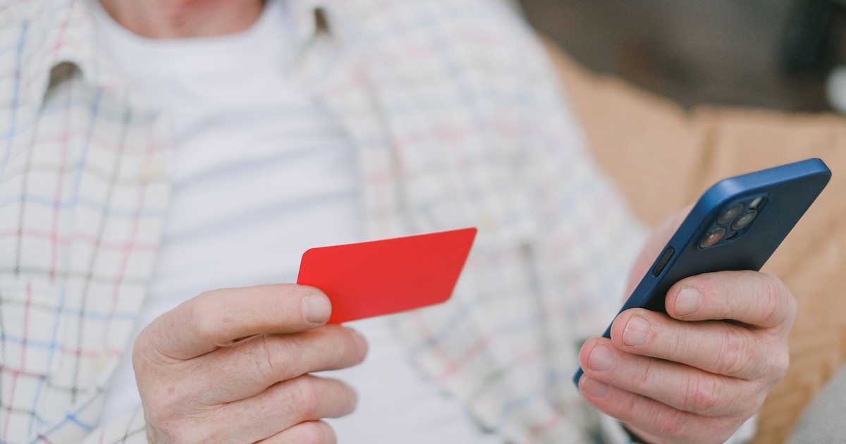 Close-up of a senior adult handling a card and smartphone for online payment.