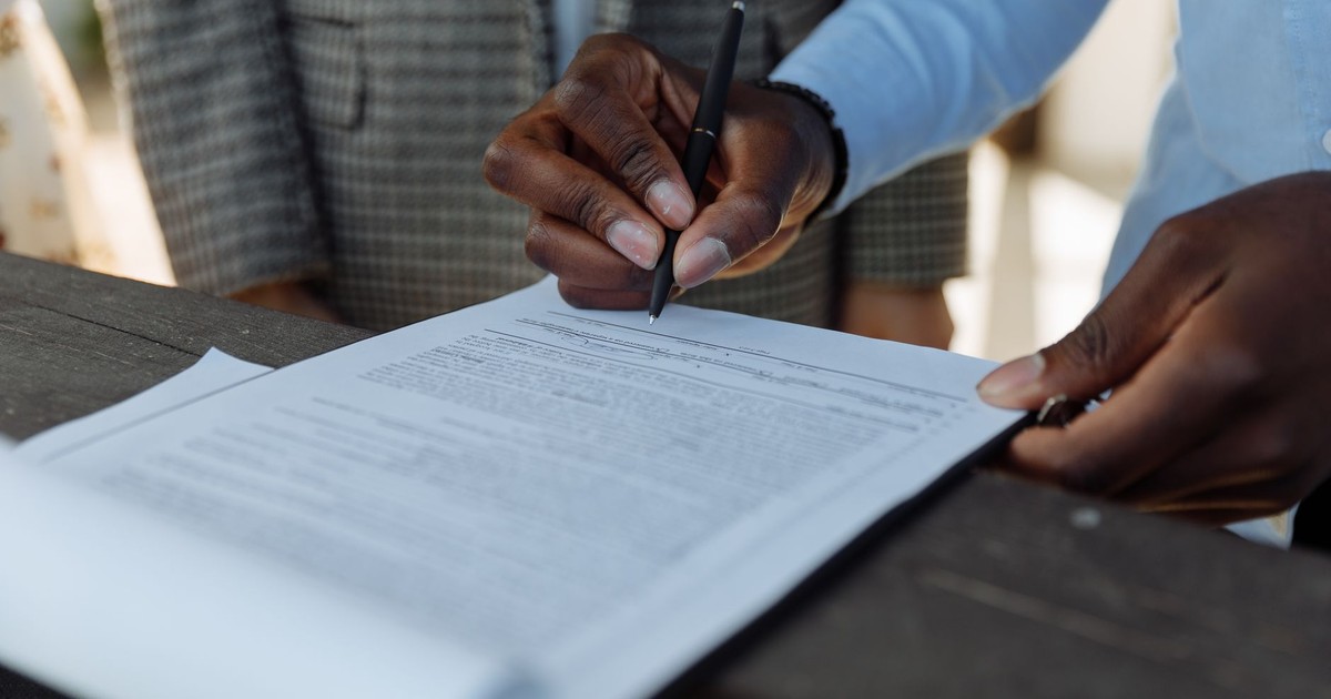 Close-up of business professionals signing a document with a pen indoors.