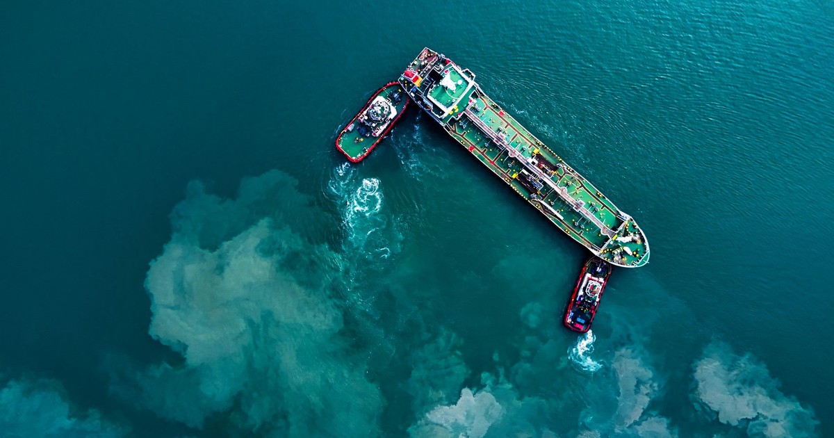 Top-down view of cargo ship and tugboats in turquoise waters near Butterworth, Malaysia.