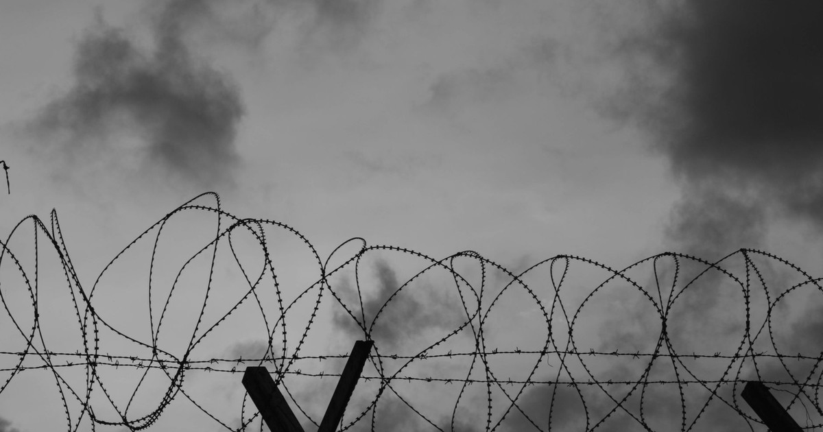 A dramatic black-and-white image showing barbed wire silhouetted against a cloudy sky.