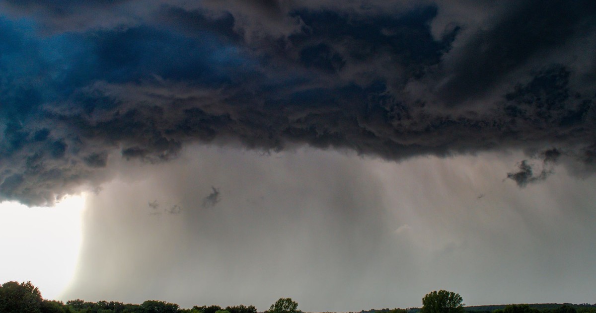 Dark stormy clouds loom over a serene green meadow, signaling an approaching storm.
