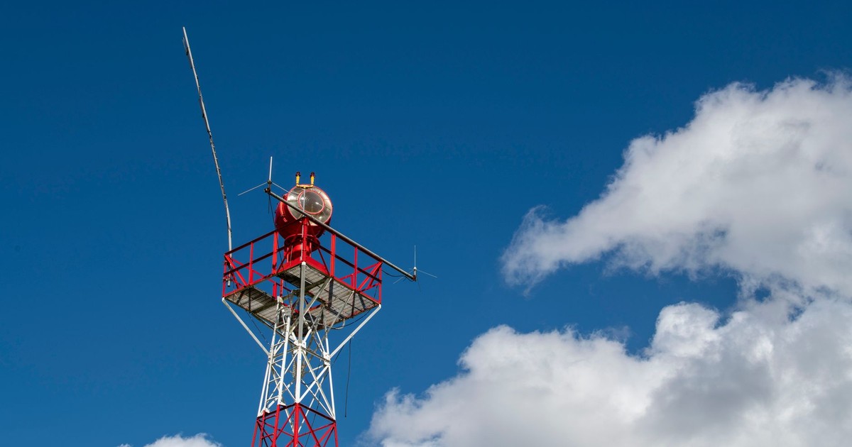 Low-angle shot of a red and white communication tower reaching into a bright blue sky with fluffy clouds.
