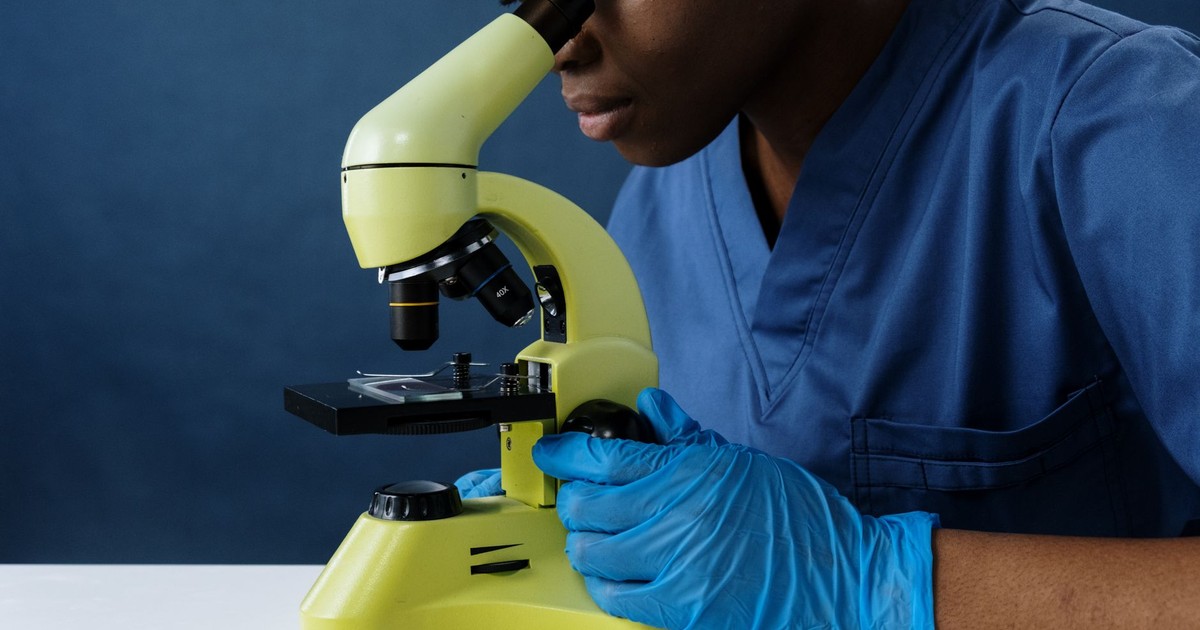 Scientist in scrubs using a microscope in a lab setting.