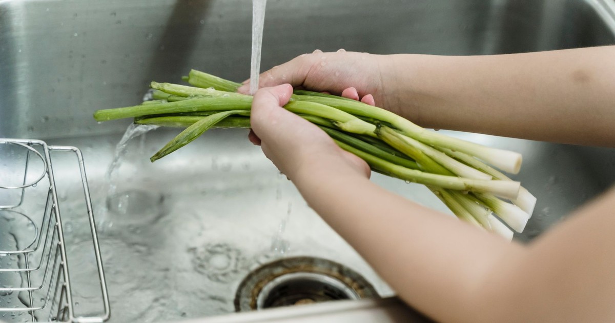 Hands washing fresh leeks under running water in a kitchen sink, ensuring hygiene and cleanliness.