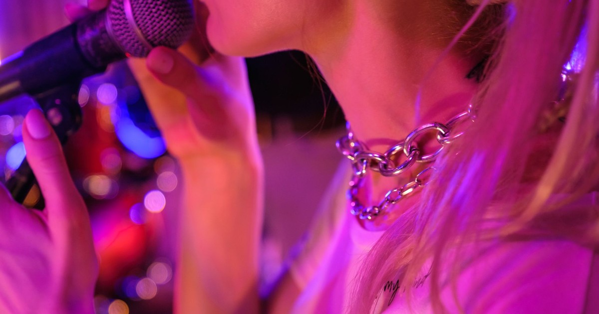 Close-up of a woman singing into a microphone with vibrant stage lighting.