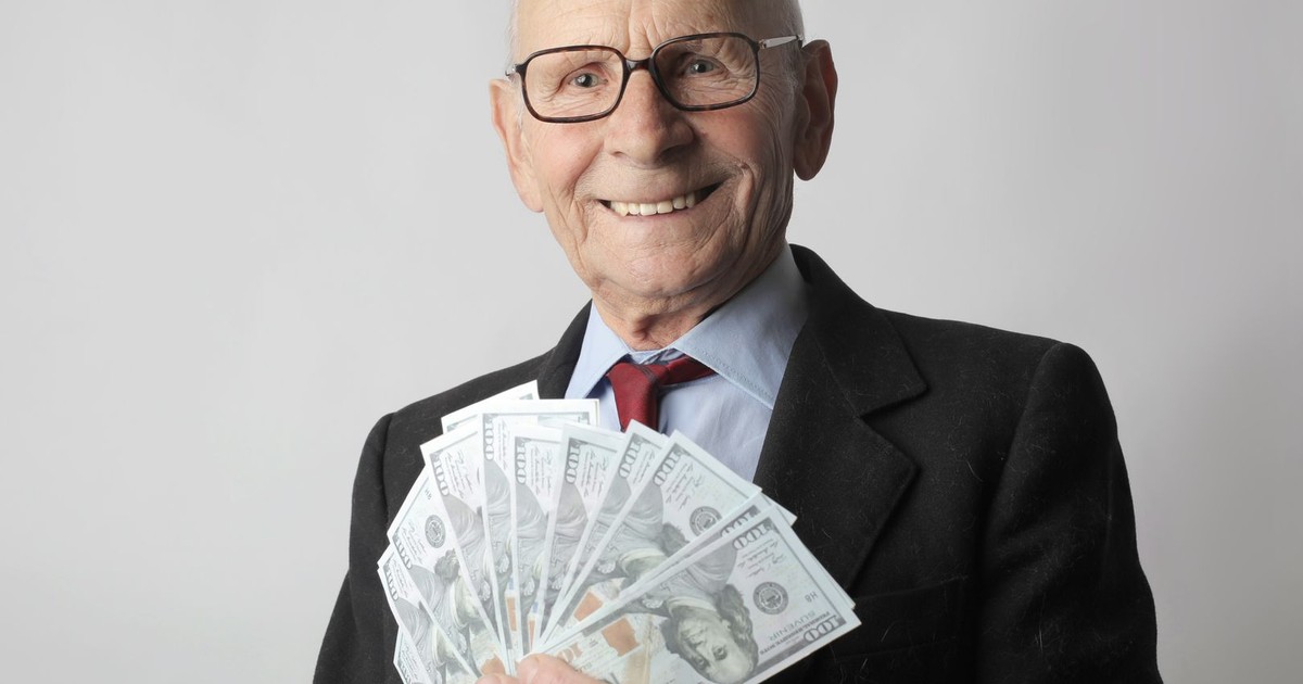 Senior man in a suit with glasses holding US dollars, symbolizing wealth and savings.