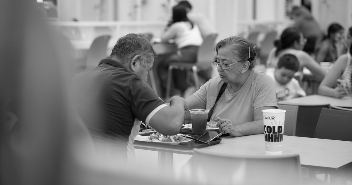 Elderly couple enjoying a meal at a fast food restaurant in a bustling food court.