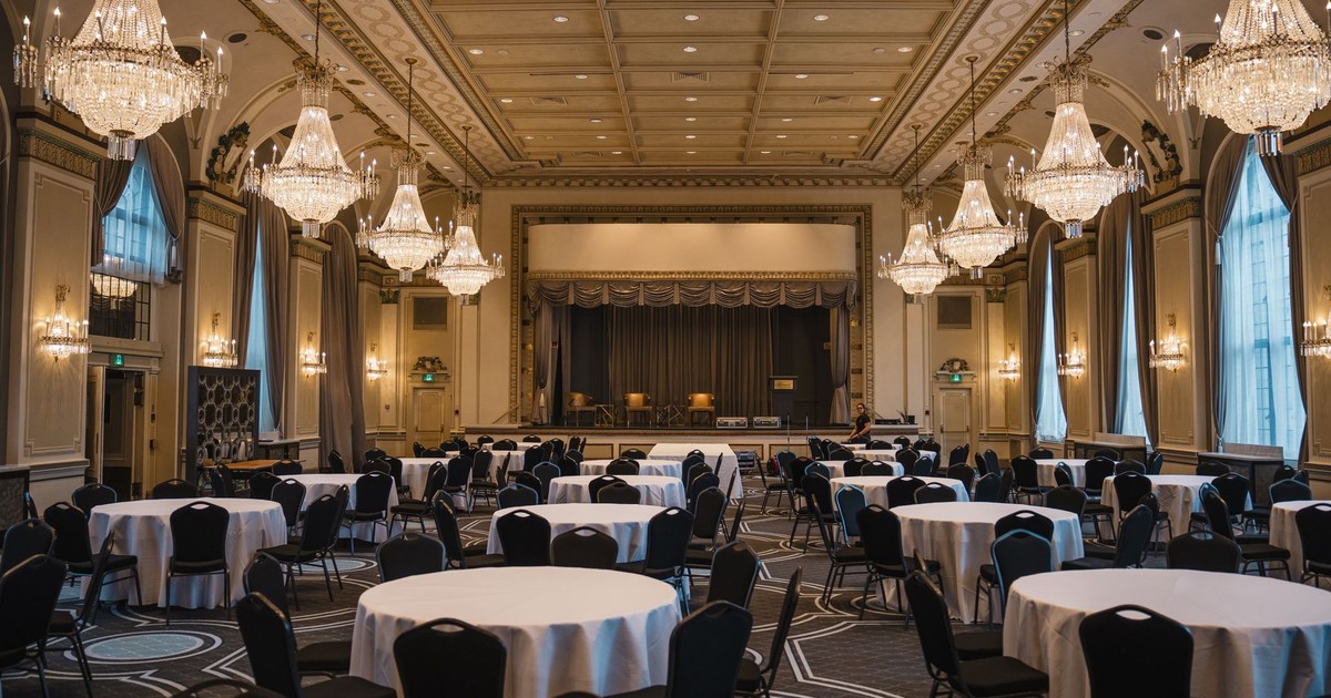 Luxurious empty banquet hall in Québec featuring round tables, elegant chandeliers, and classical architecture.