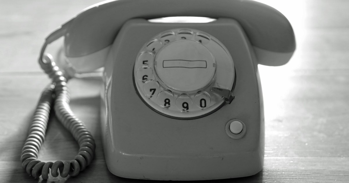 High contrast black and white image of a vintage rotary phone on a wooden surface emphasizing nostalgic communication.