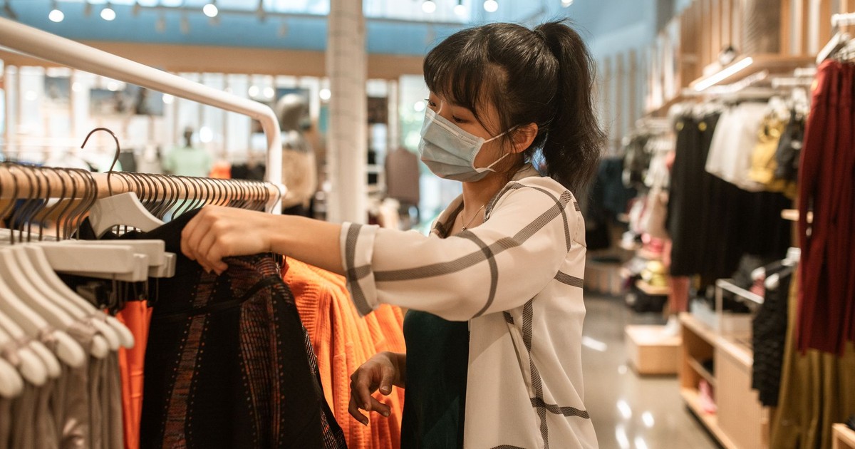 Woman wearing a face mask shopping for clothes in a department store.