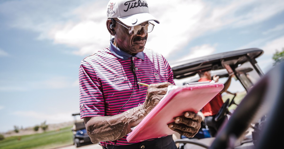 Senior man in golf attire writing on clipboard outdoors on a sunny day.