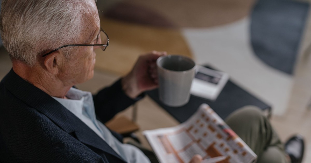 Senior man enjoying coffee while reading a newspaper indoors, exuding calm and relaxation.