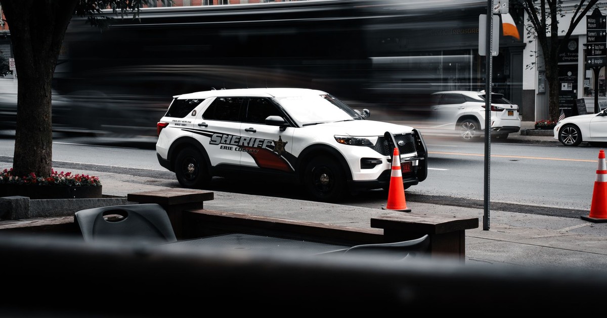 Sheriff's vehicle parked on a bustling city street with traffic motion blur.