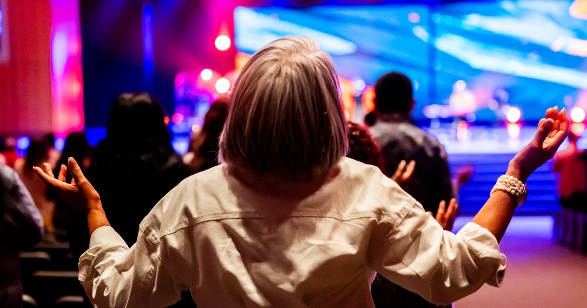 A vibrant indoor worship service with people raising hands in praise and colorful stage lighting.