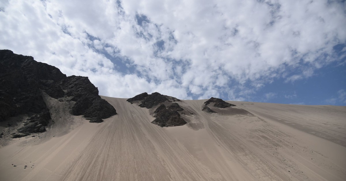 Expansive sand dunes under a blue sky and scattered clouds, showcasing natural beauty and wilderness.