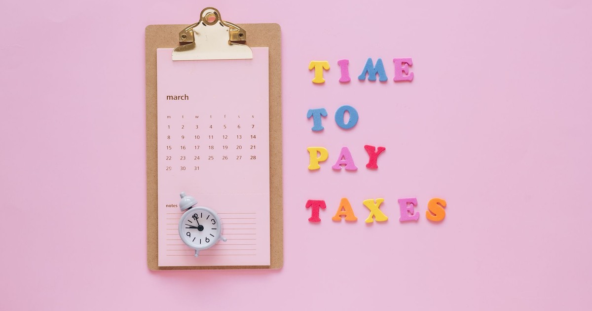 A flat lay of a March calendar and 'Time to Pay Taxes' letters on a pink background.