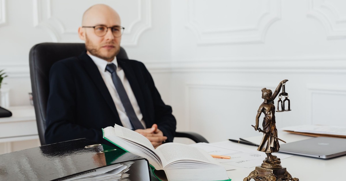 Bald lawyer in office sitting with legal documents and Justice statue.