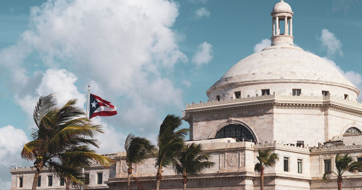 Stunning shot of Puerto Rico's Capitol with palm trees and flag under a bright blue sky.