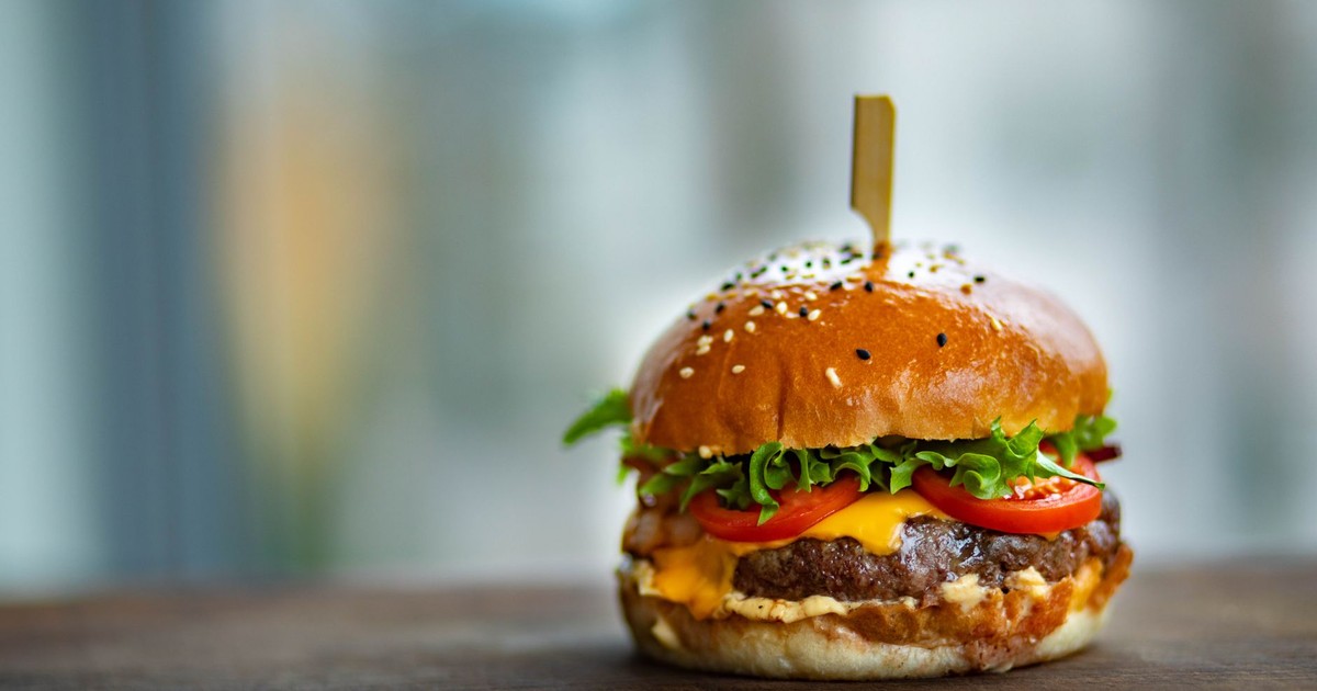 Mouthwatering cheeseburger with fresh tomatoes and lettuce on a wooden surface.