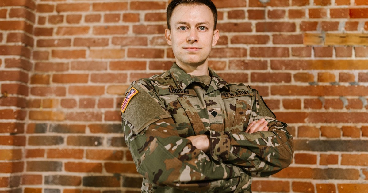 US Army soldier standing confidently with arms crossed against a brick wall, embodying pride and honor.
