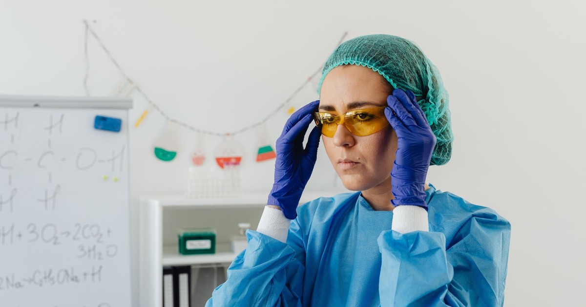 Woman scientist in protective gear adjusting goggles in a laboratory setting, focusing on preparation.