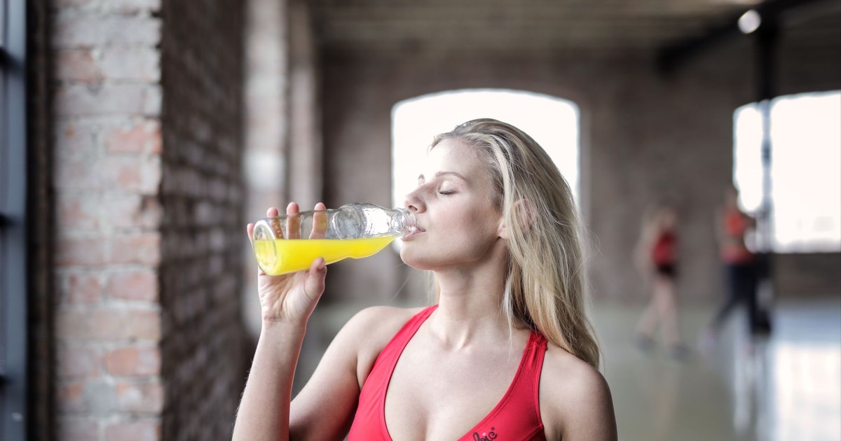Athletic woman enjoying a refreshing drink in a gym environment, promoting fitness and hydration.