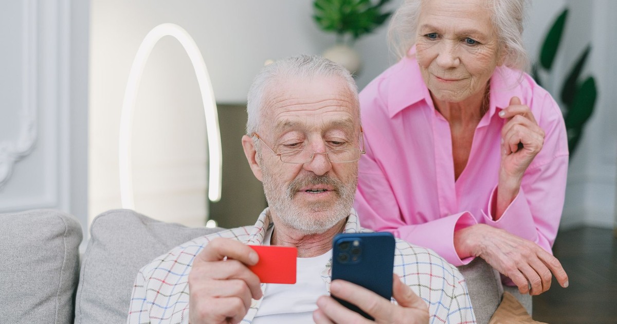 Elderly couple using smartphone and credit card for online shopping at home.