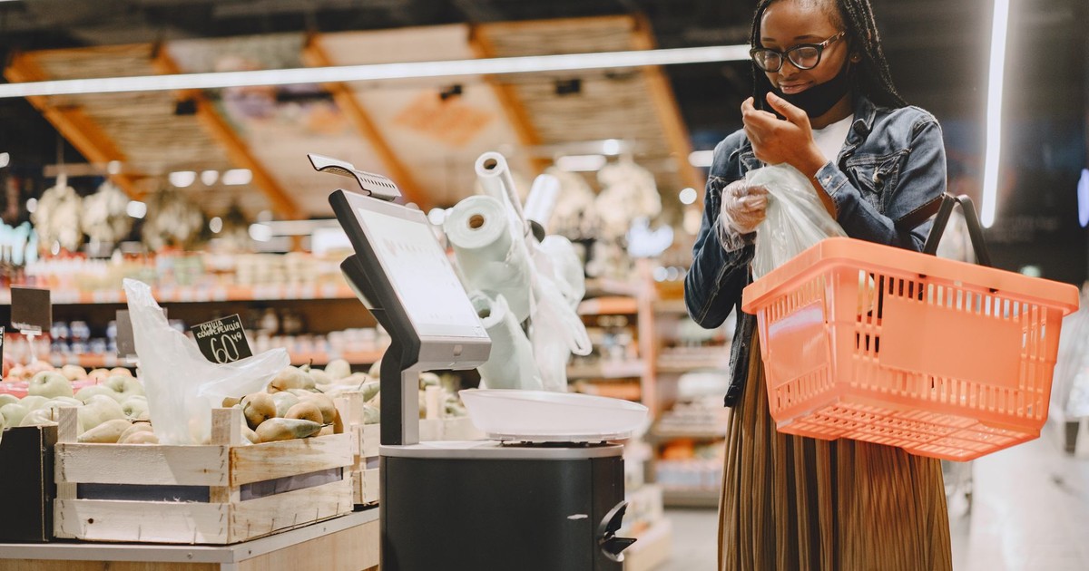 A woman shopping in a supermarket, checking items with a basket in hand.