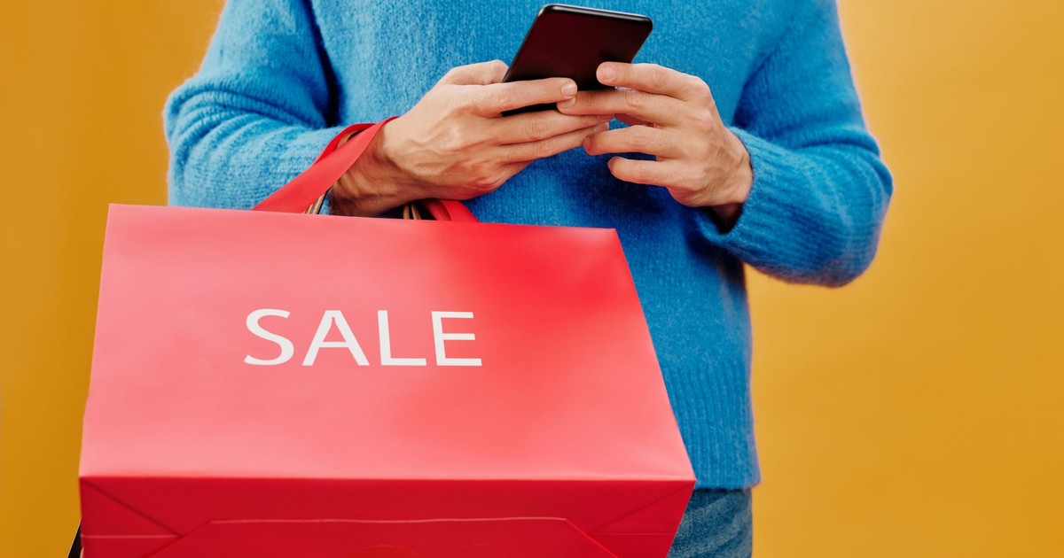 Close-up of a man holding a sale bag and smartphone, symbolizing shopping and discounts.