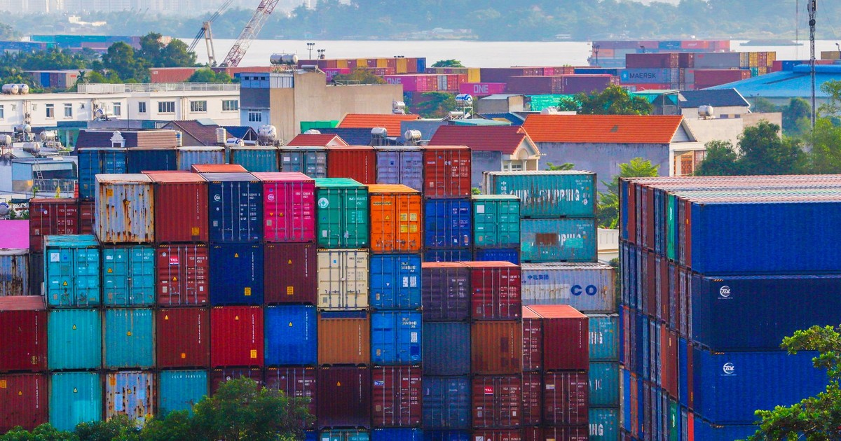 Vibrant stacked cargo containers at a bustling port with urban skyline in background.