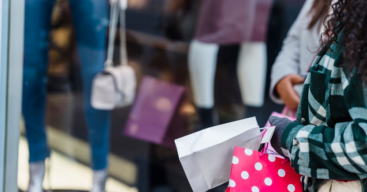 Crop anonymous women friends in stylish clothes standing with shopping bags near counter of boutique in daytime