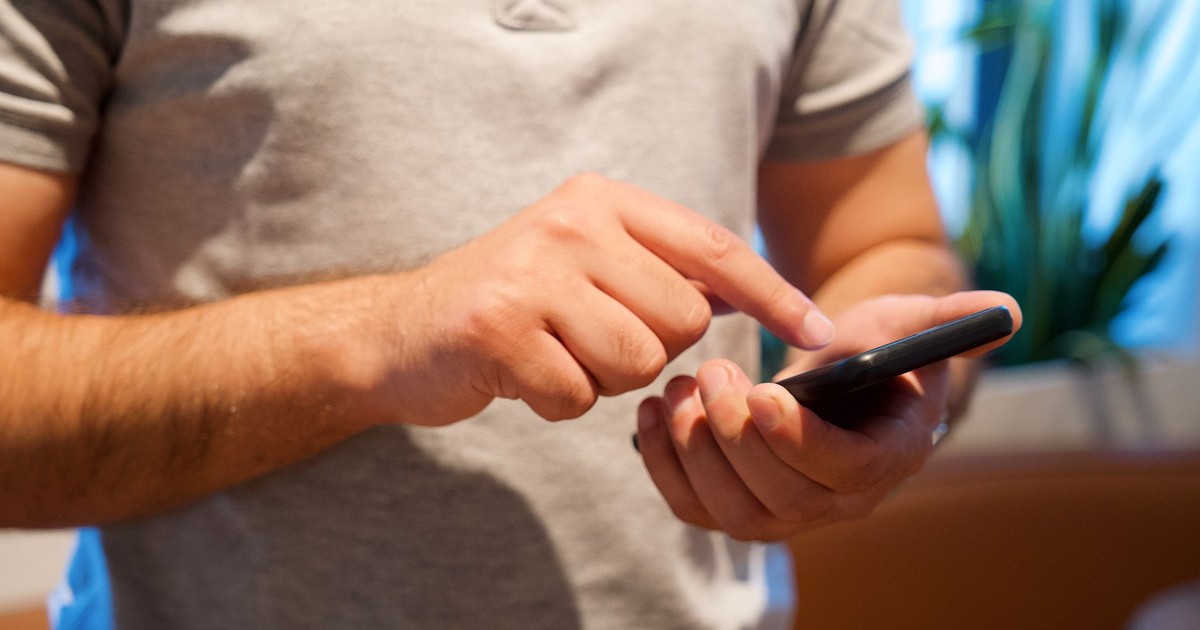 Adult male using smartphone in a bright indoor setting, focusing on the device and interaction.
