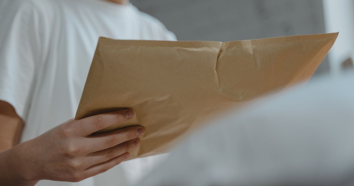 Close-up of a person holding a brown paper envelope, highlighting courier services or postal delivery indoors.