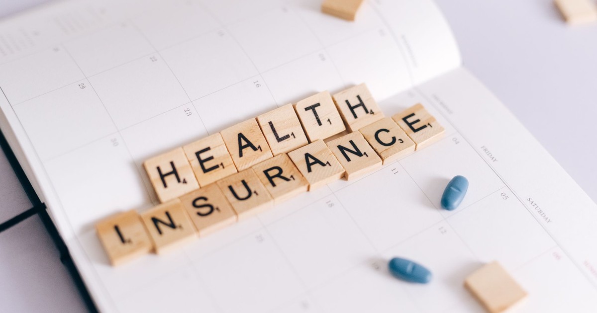 Close-up of health insurance spelled out with Scrabble tiles on a planner, alongside medication pills.