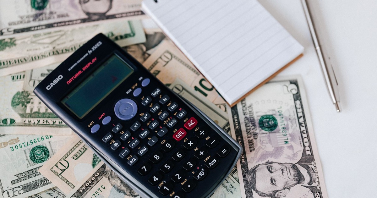 From above electronic calculator and notepad placed over United States dollar bills together with metallic pen for budget planning and calculation