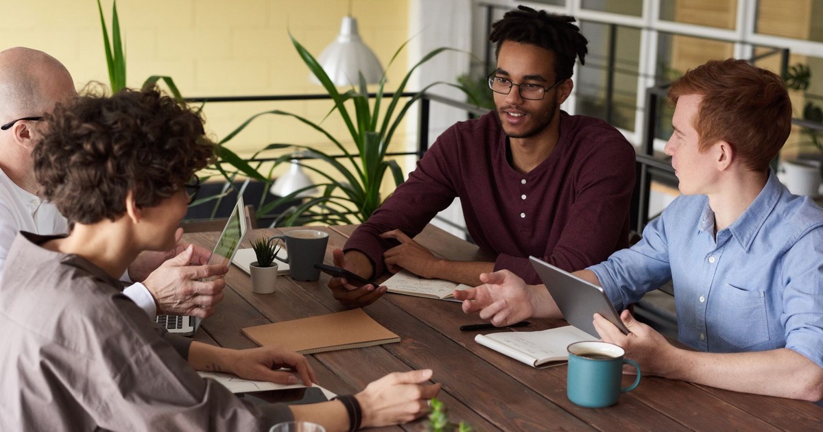 A diverse group of colleagues brainstorming at a wooden table in a modern indoor office setting.