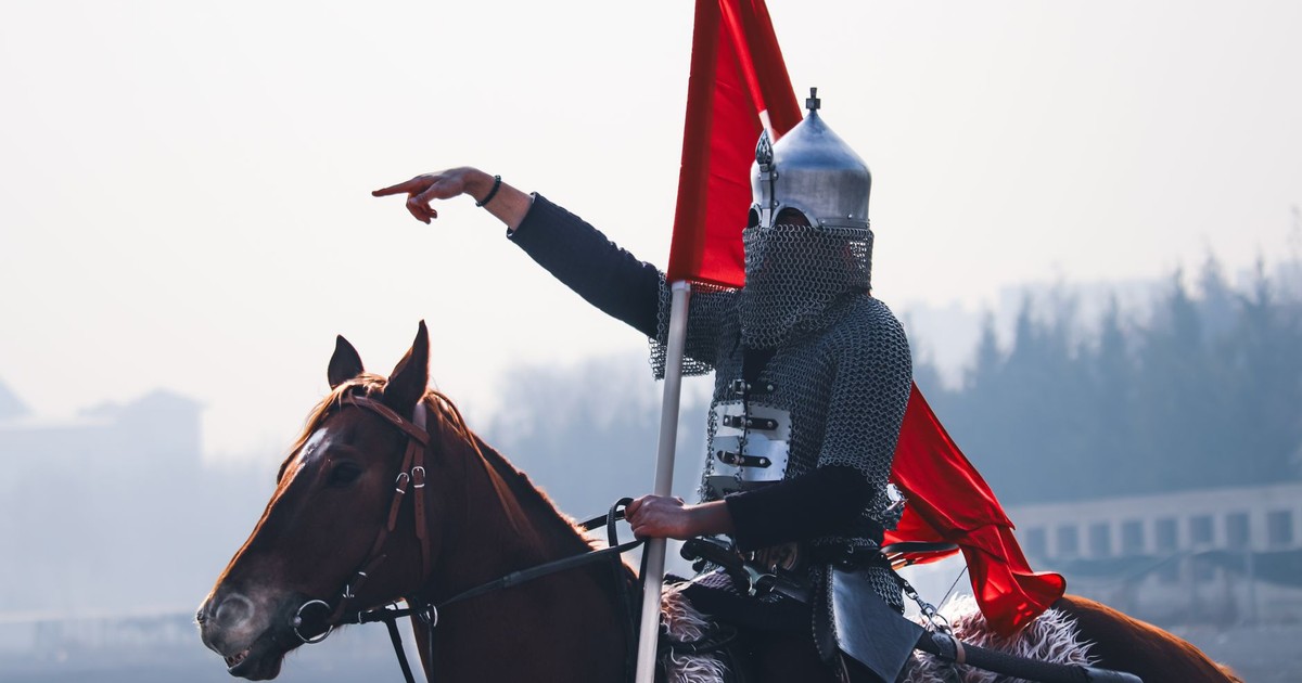A medieval warrior in armor riding a horse holding a flag, outdoors in Konya, Türkiye.